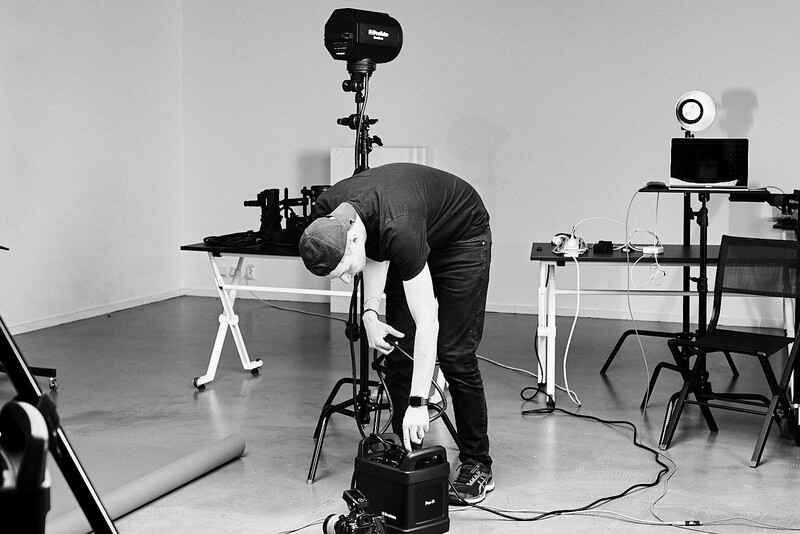 Photographer bent over a stationary bike in a studio setup with professional lighting equipment and monitors.