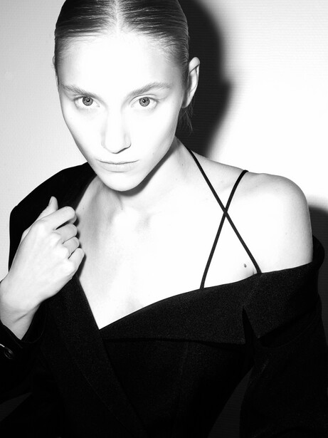 Woman in black off-shoulder top against neutral background in high-contrast black and white portrait.