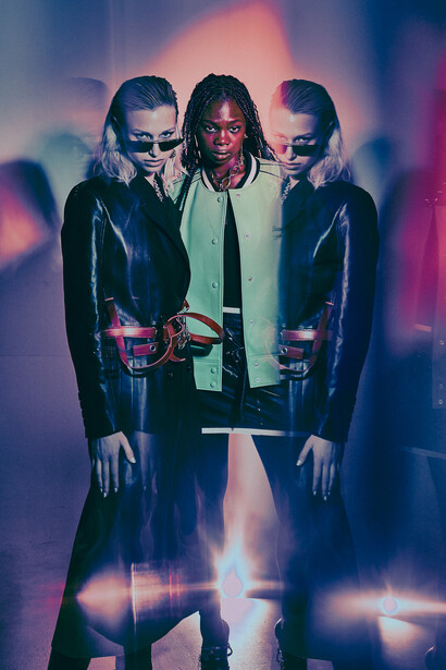 Three figures in leather jackets positioned symmetrically against a moody, colorful light backdrop.