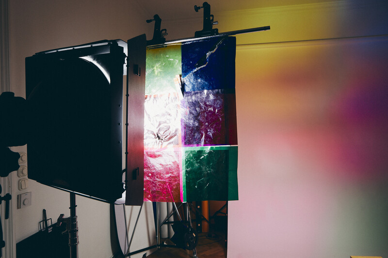 Professional lighting setup with colorful gels creating vibrant projected light on white wall during studio session.