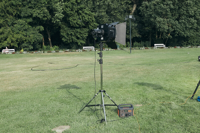Outdoor lighting equipment setup on tripod in open field with trees in background.