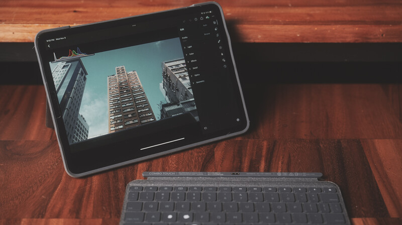 iPad displaying architectural photography of tall buildings shot from below against a blue sky, positioned next to a wireless keyboard on a wooden desk.