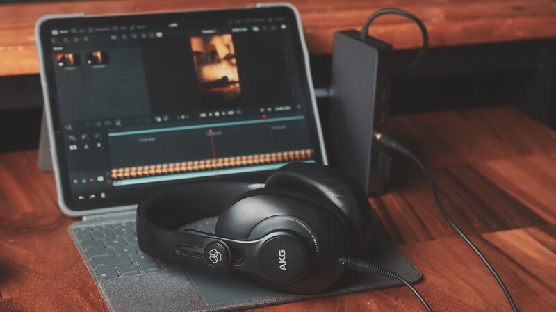 Over-ear headphones resting on a gray fabric surface next to a laptop displaying video editing software with an orange color grade.