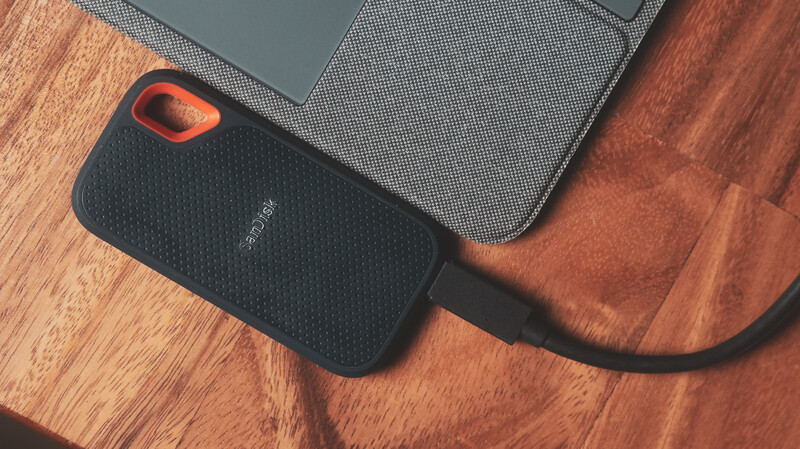 SanDisk Extreme portable SSD with orange and black design on wooden surface next to laptop.