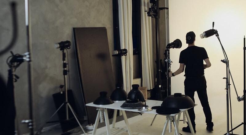 Photographer adjusting studio lighting setup with multiple light stands and reflectors in a controlled studio environment.