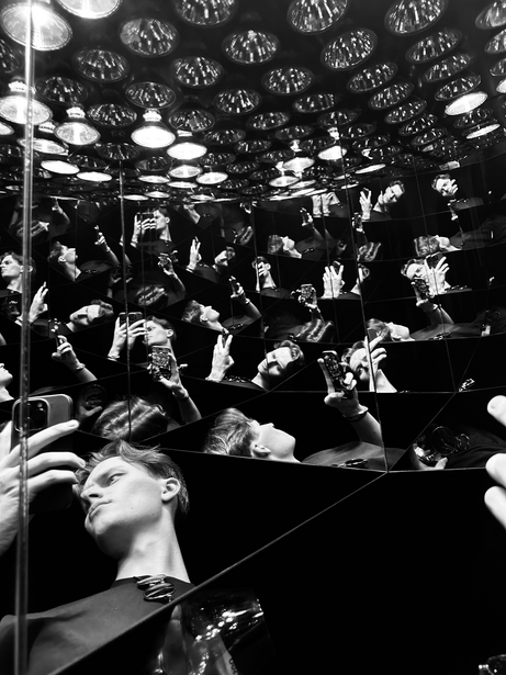 Black and white photograph of a crowded indoor space with overhead lighting fixtures and multiple people looking upward.