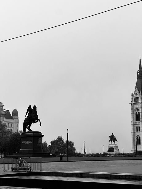 Equestrian statue in foreground with neoclassical buildings and church spire across water in background.