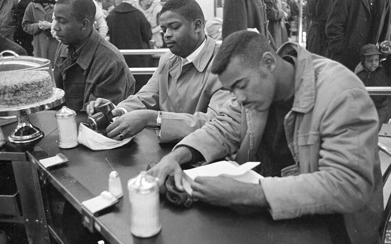 Black and white photograph of men seated at a counter eating and drinking.