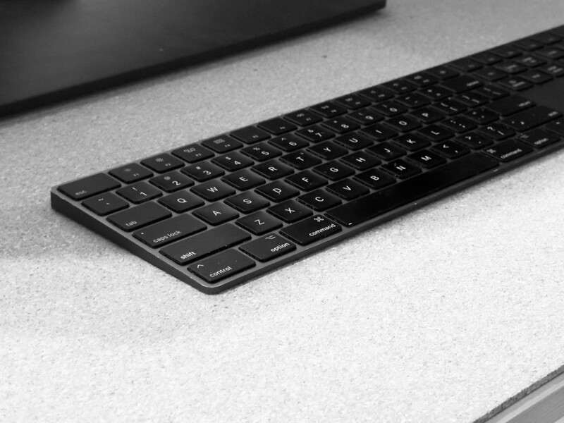 Black wireless keyboard on light gray surface with blurred background elements.