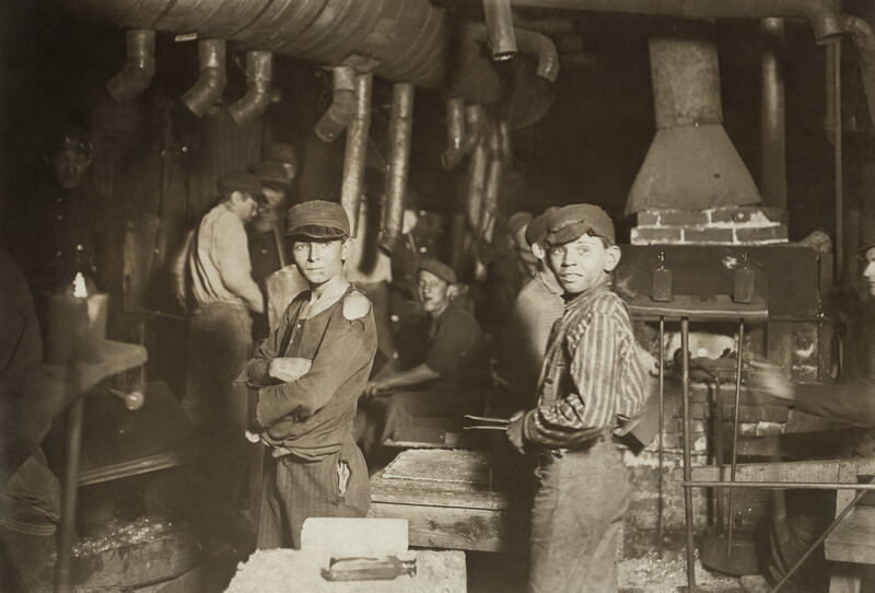Young workers in a factory interior with industrial equipment and pipes, shot in sepia tones.