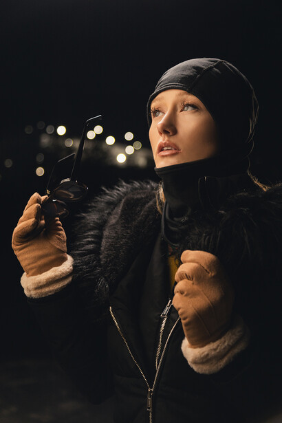Person in dark winter clothing against blurred bokeh background at night.