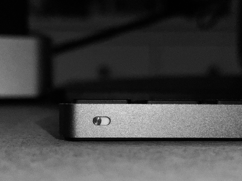 Close-up of a metallic rectangular object with a small circular button or indicator on its surface, photographed in monochrome lighting.