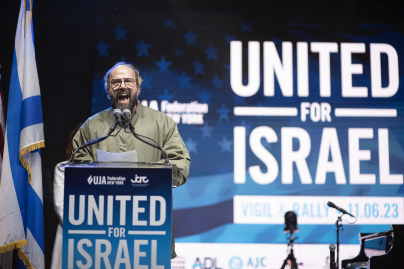 Man speaking at podium with Israeli flag and 'United for Israel' branding visible behind him.