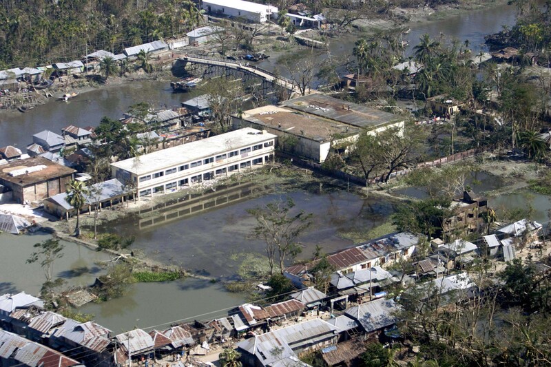 Aerial view of a white multi-story building surrounded by waterways and informal structures in a dense riverside settlement.