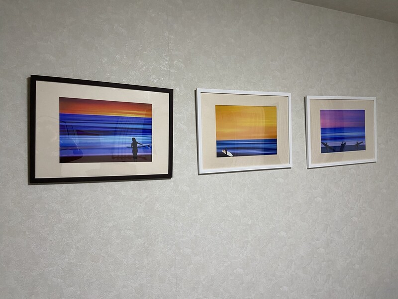 Three framed landscape photographs with vibrant sunset and ocean horizons displayed on a white textured wall.