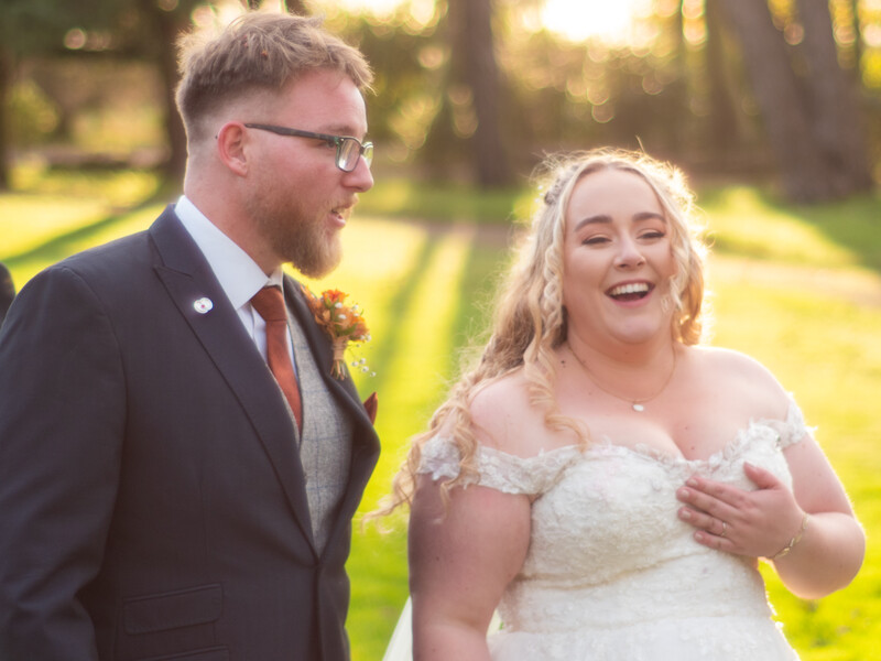 Bride and groom laughing together outdoors during golden hour in a tree-lined setting.