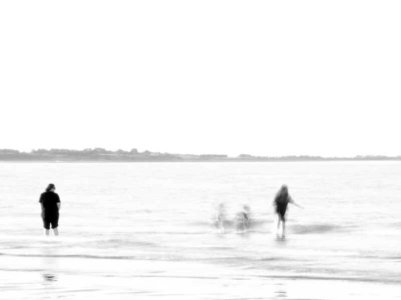Multiple figures wading and surfing in ocean waves with motion blur effect.