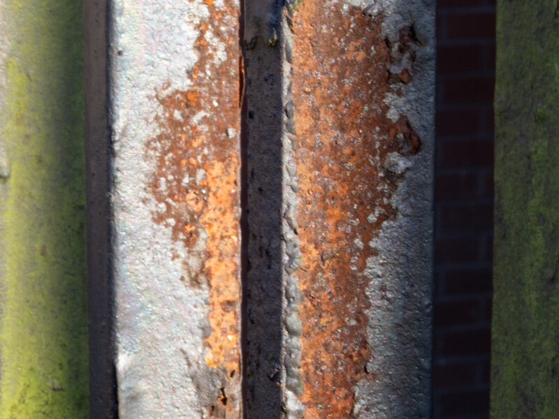 Close-up of two parallel metal pipes with varying rust and lichen growth patterns.