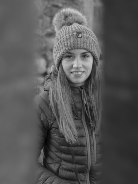 Young girl wearing a knit beanie and puffy jacket, smiling at camera in black and white portrait.