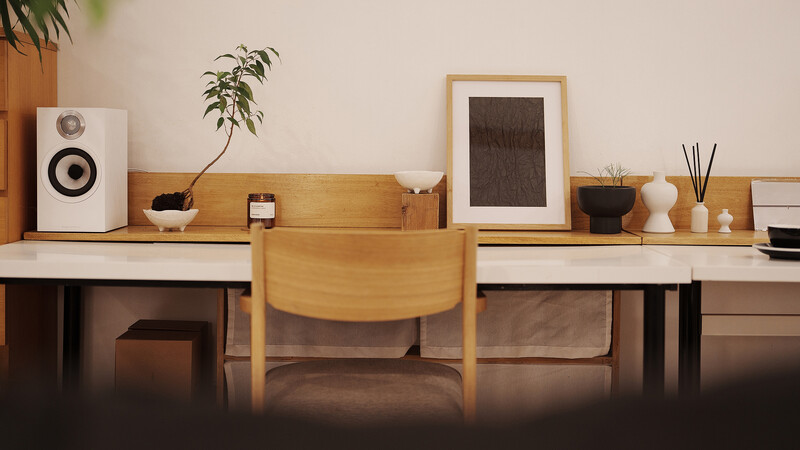 Minimalist wooden desk workspace with speaker, plants, and framed artwork on floating shelves.