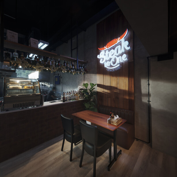Modern bar interior at night with neon sign, wooden table with chairs, and backlit shelving displaying bottles.