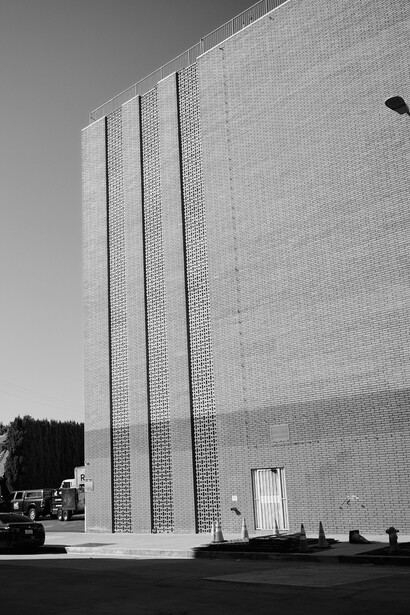 Modernist brick building facade with three tall vertical ribbed columns against clear sky.
