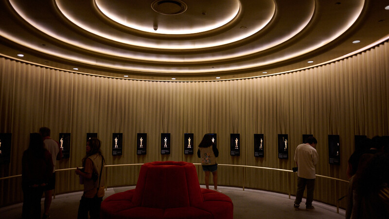 Modern circular gallery with concentric ceiling rings, warm ambient lighting, red central seating, and illuminated wall displays.