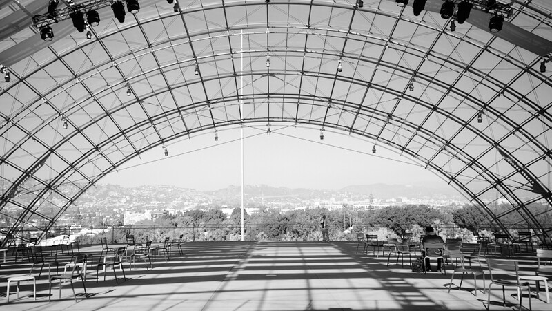 Interior of a curved architectural structure with geometric grid framework overlooking a distant cityscape.