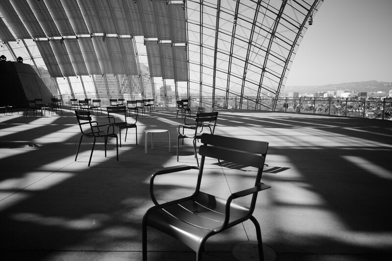 Modern architectural interior with geometric glass ceiling and black metal chairs casting sharp shadows across floor.