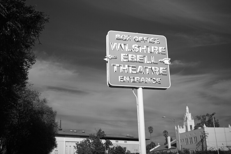 Vintage neon sign for a theater entrance against dramatic cloudy sky, photographed in black and white.