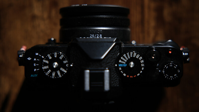 Top-down view of a black rangefinder camera with dual dials, aperture and shutter speed controls visible.