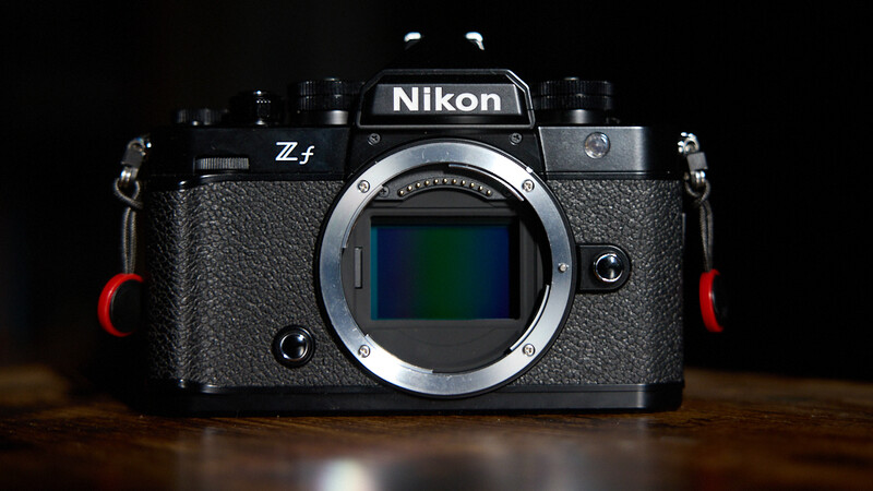 Nikon Zf mirrorless camera body displayed front-on against a dark background with dramatic side lighting.
