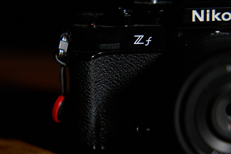 Close-up of a Nikon Z f camera body showing textured grip and red shutter release button against dark background.