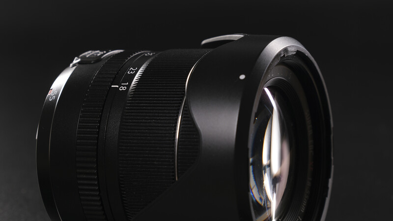 Black camera lens with focus ring and aperture markings against dark background.