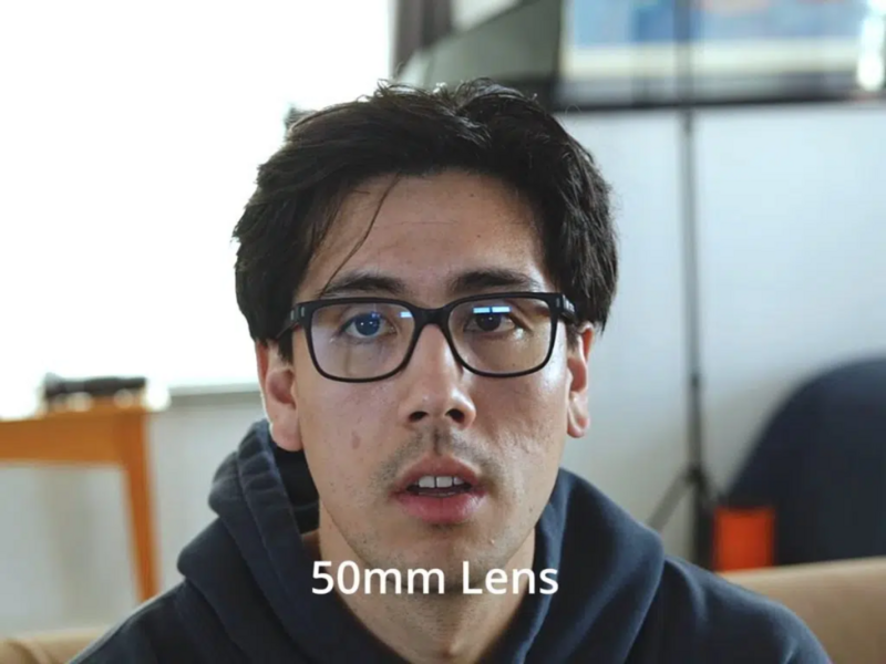 Man wearing glasses in an indoor office setting with text overlay reading '50mm Lens'.
