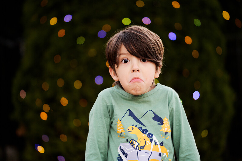 Young child in green shirt with pouty expression against blurred bokeh background.