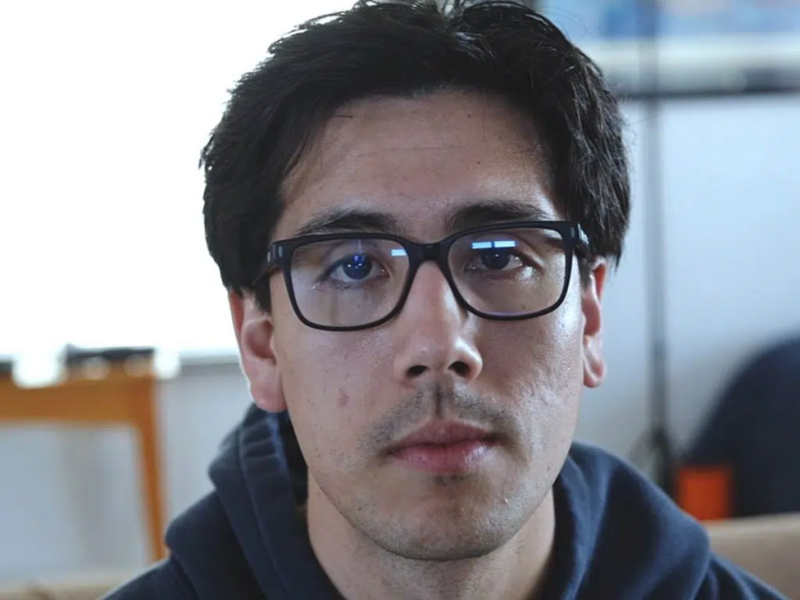 Man wearing glasses and dark hoodie looking at camera in indoor setting.