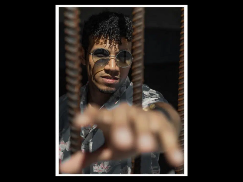 Shirtless man with geometric face paint and dark braided hair looking toward camera.