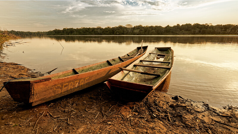 Two weathered boats beached on sandy shore beside calm water at golden hour.