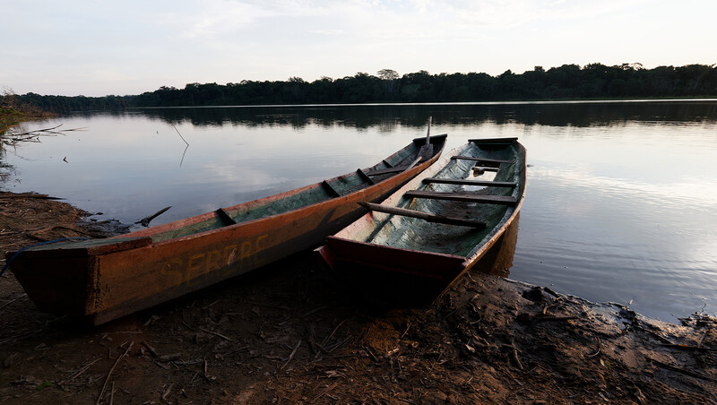 Two weathered wooden fishing boats beached on muddy shore beside calm river.