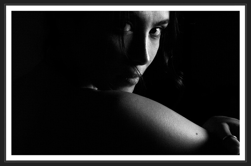 Woman in dramatic side lighting against dark background, looking toward camera.