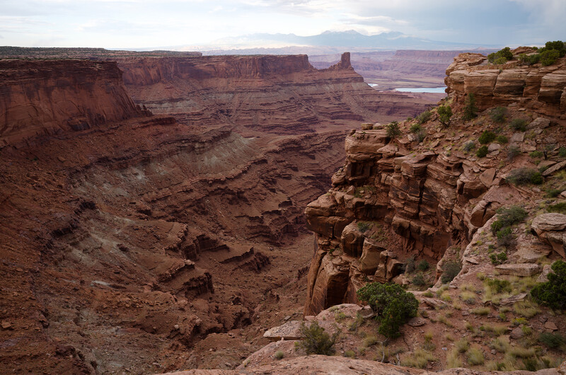 Layered desert canyon landscape with eroded red rock formations and sparse vegetation.