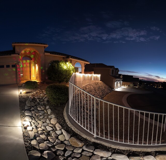 Modern home exterior at twilight with warm architectural lighting and curved metal railing along stone pathway.