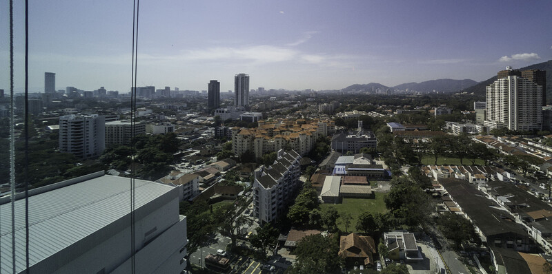 Aerial cityscape view from a high-rise window showing urban sprawl, green spaces, and mountains in the distance.