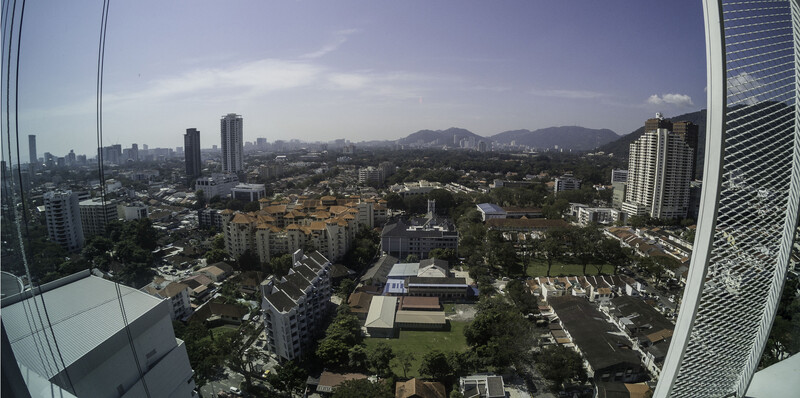 Aerial cityscape taken from a high-rise building showing urban sprawl, parks, and distant mountains under partly cloudy sky.