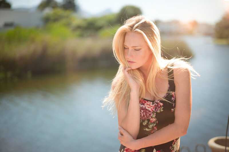 Blonde woman gazing downward by a waterway during golden hour.