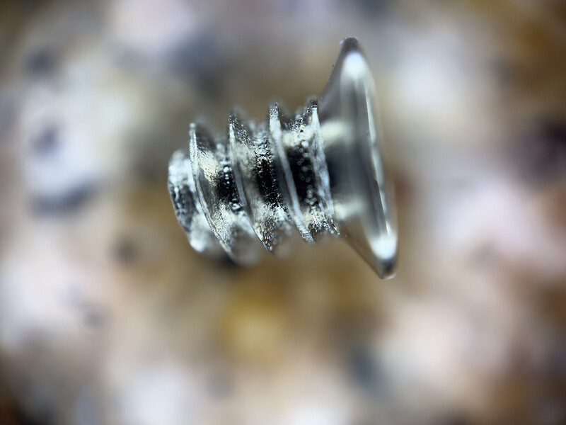 Macro photograph of a metal screw with frost or ice crystals coating its threads and head.