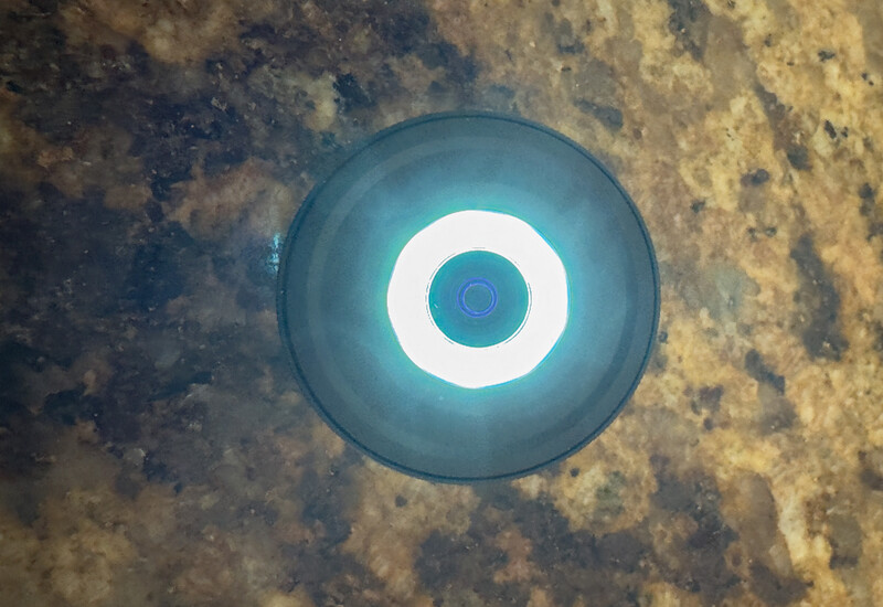 Illuminated circular device with concentric white and teal rings mounted on weathered, discolored concrete surface.