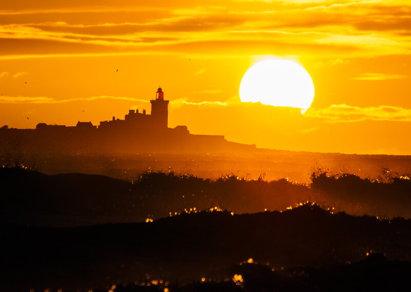 Silhouetted hilltop castle against a massive golden sunset sun.