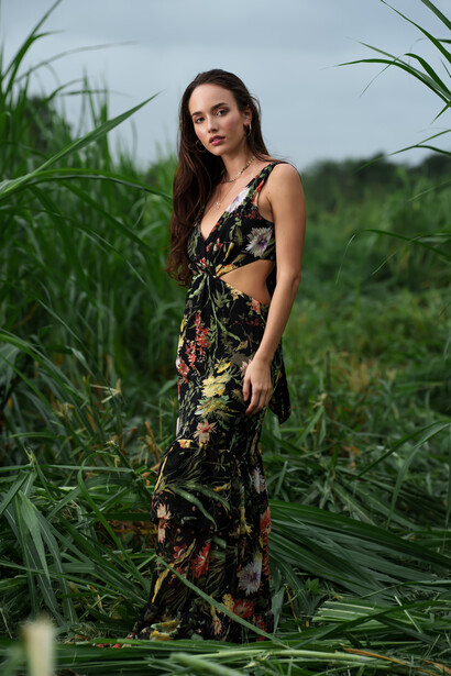 Woman in floral dress standing among tall green plants in an outdoor field.